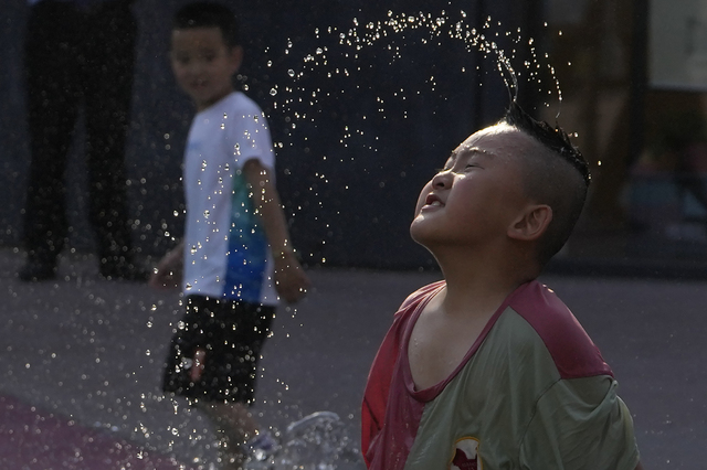 Barn i Beijing svalkar sig i en fontän under fredagen då temperaturen låg på rekordhöga 39,4 grader i kinesiska huvudstaden.