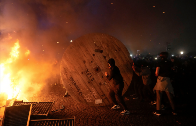 Demonstranter rullar in en kabeltrumma i en brinnande barrikad.