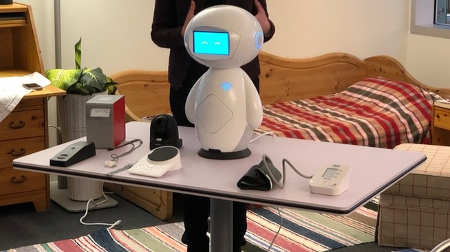 Telenor viser frem hvordan en trådløs blodtrykkmåler, trygghetsalarmer og andre enheter kan kobles til deres nye «smarte hjemmehjelp». Den lille hvite roboten kan både ringe etter hjelp, minne deg på å ta medisiner eller spørre om alt går bra hvis den merker at du har falt