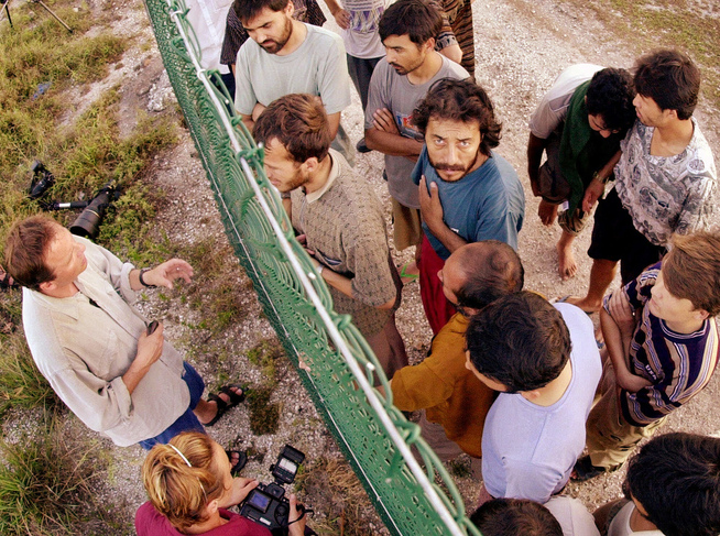 <p>BAK GJERDET: Leiren på Nauru ble etablert i 2001. I begynnelsen tillot Nauru journalister å intervjue leirbeboerne, men det endret seg raskt. Bildet viser journalister som står utenfor gjerdet for å snakke med internerte asylsøkere. FOTO: RICK RYCROFT / AP</p>
