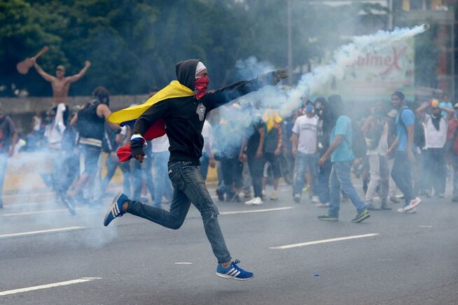 <p>PROTESTER: En mann med det venezuelanske flagget rundt ryggen avbildet under demonstrasjonene i Caracas torsdag. </p>